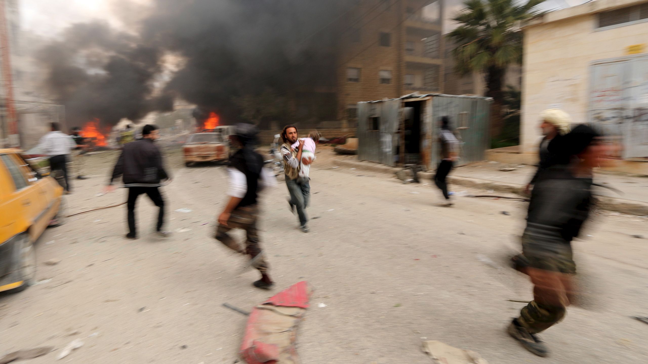 A man carrying an injured child runs from a damaged site after shelling in Idlib city.